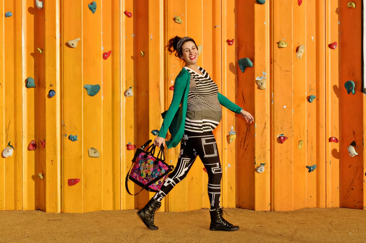 Smiling pregnant woman striding past an orange climbing wall