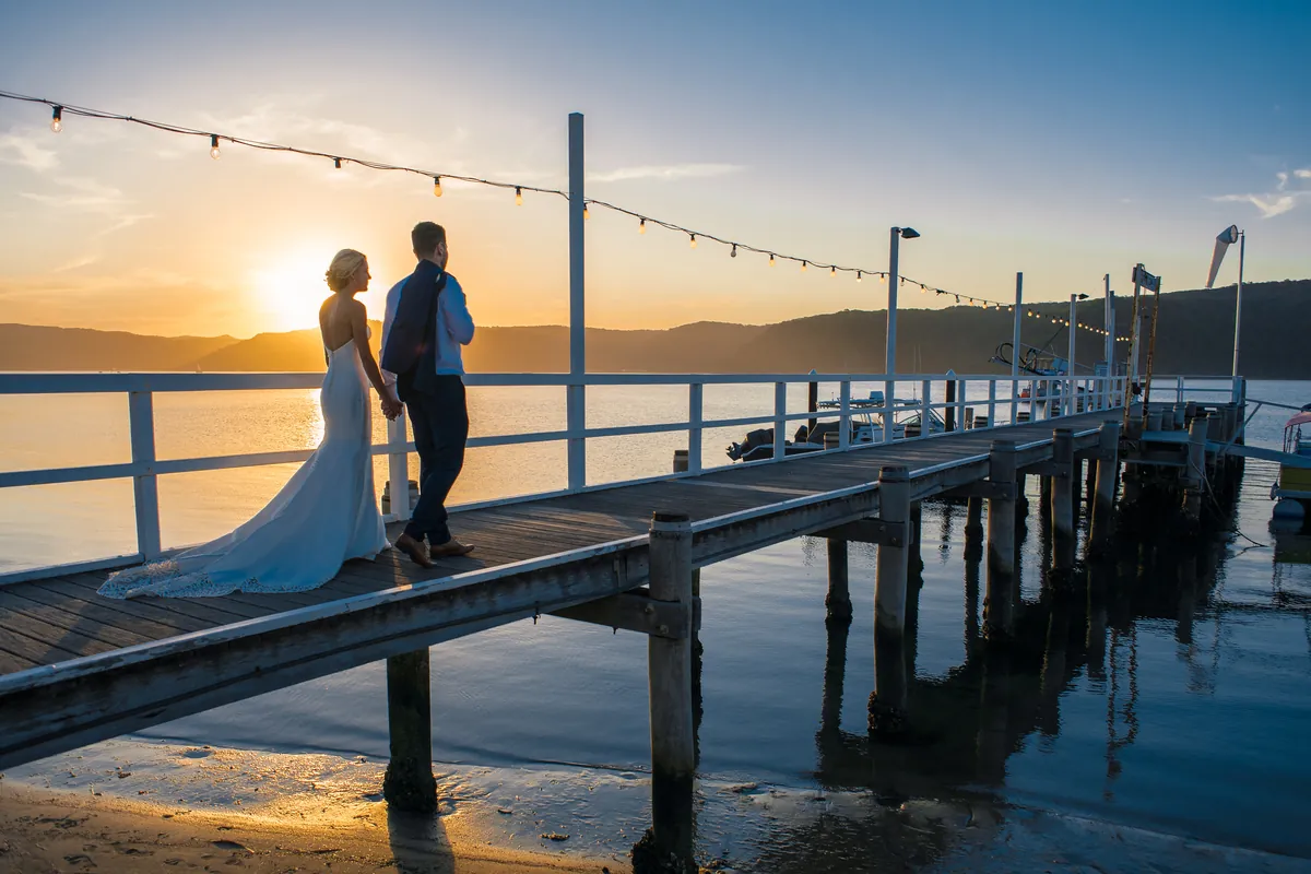 Bride and groom walking along a jetty at sunset